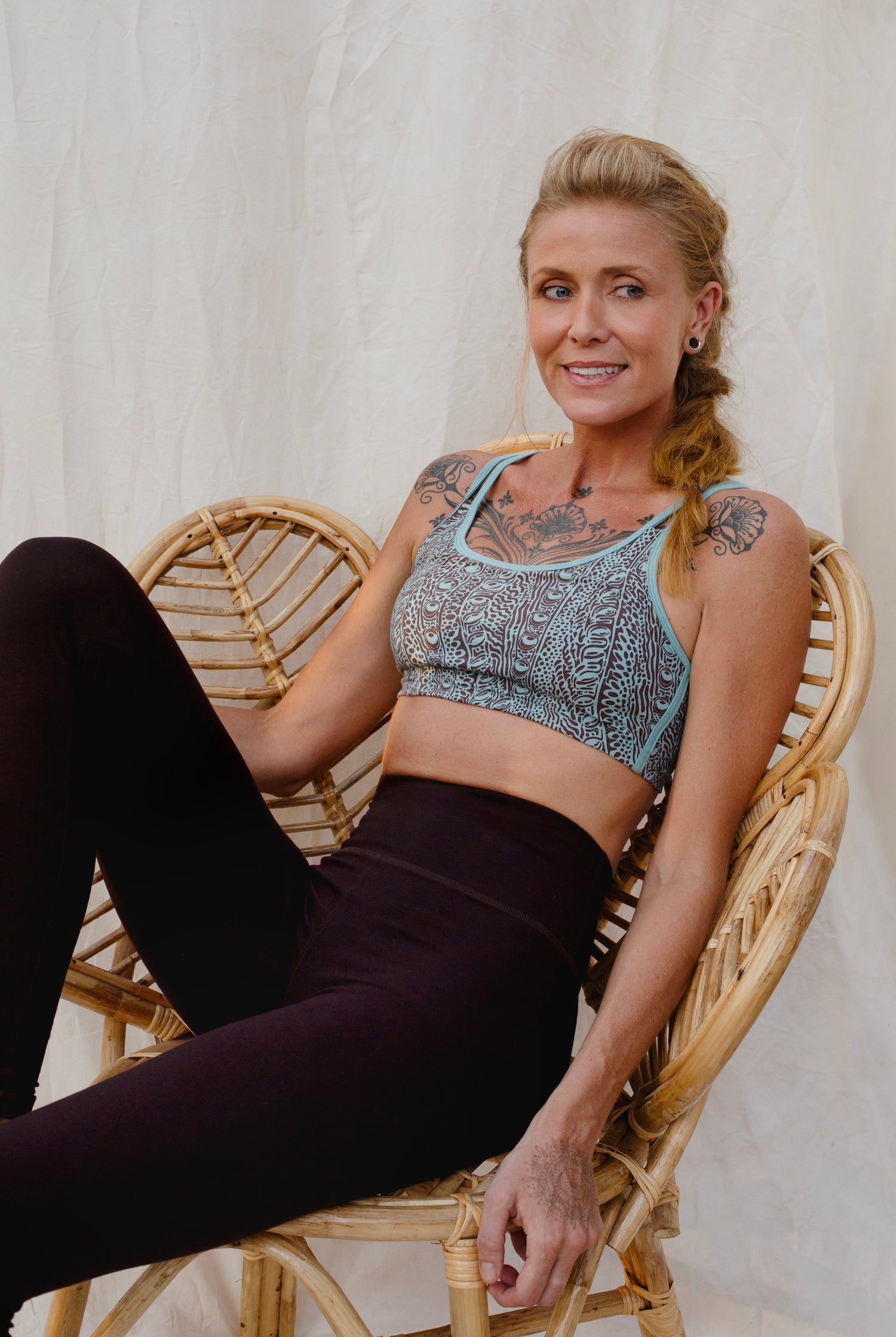 Woman sitting on a wicker chair wearing an Argus patterned sports bra and brown leggings.