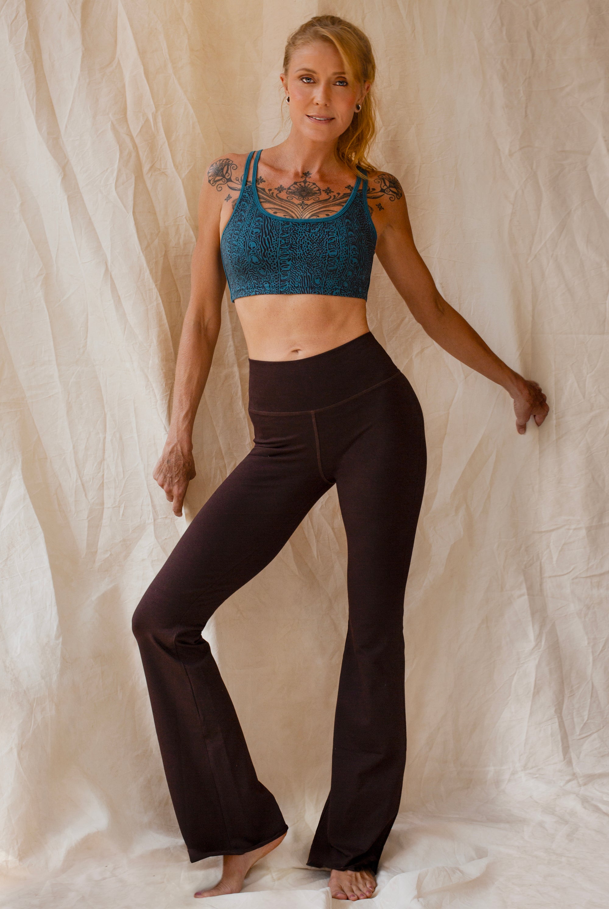 Woman wearing a tosca Argus sports bra and brown flared leggings against a beige curtain background