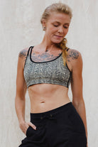 Woman wearing a cream black Argus patterned sports bra and black training pants against a light background