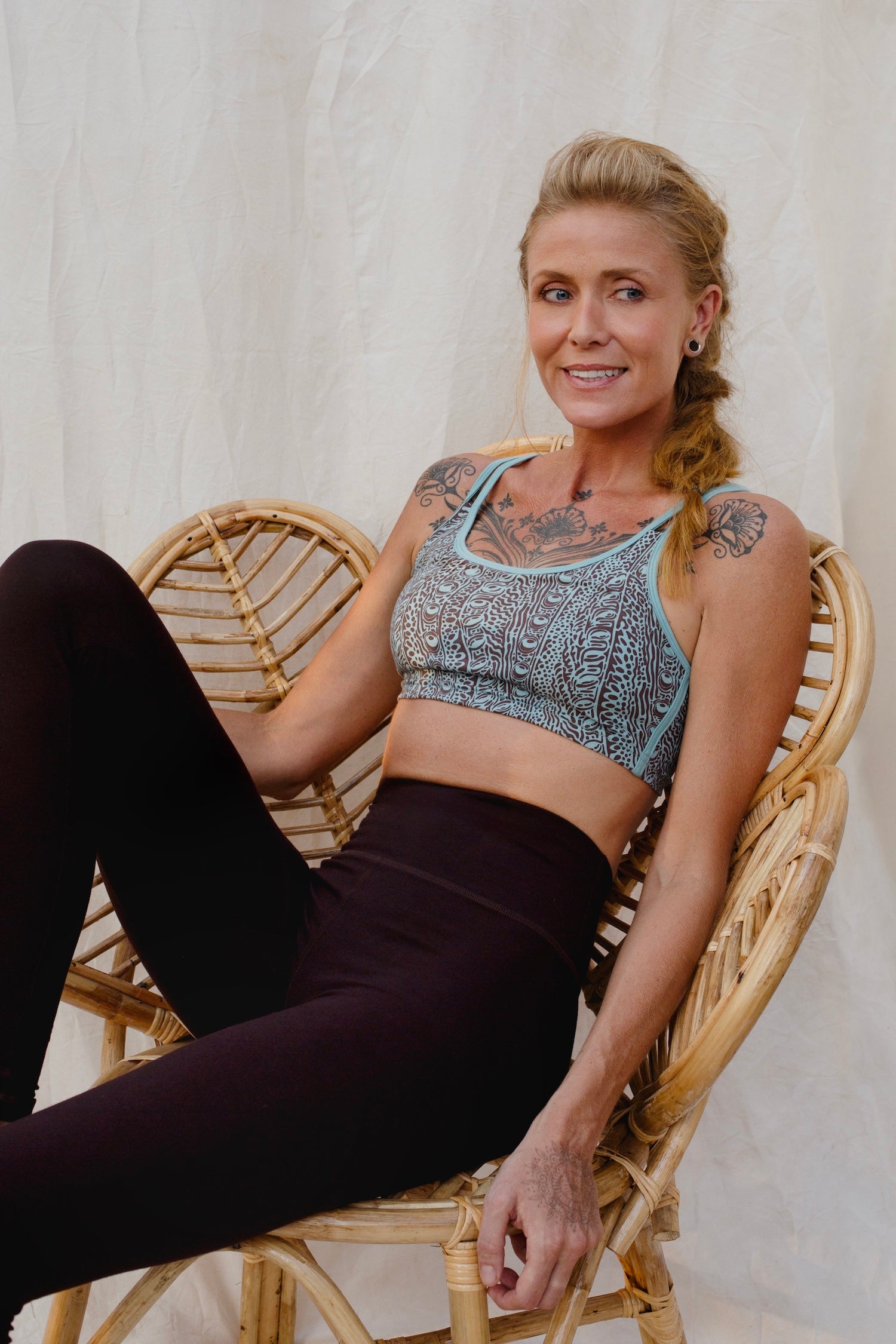 Woman sitting on a wicker chair wearing an Argus patterned sports bra and brown leggings.