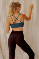 Woman wearing a tosca Argus sports bra and brown leggings shown from the back, against a textured beige background