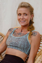 Woman with tattoos wearing an Argus patterned sports bra with a brown leggings sitting on a wicker chair 