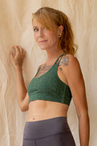 Woman wearing a green Argus sports bra and gray leggings against a beige wall.