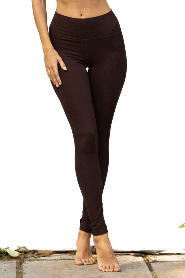 Woman in brown athletic leggings standing outdoors with greenery.