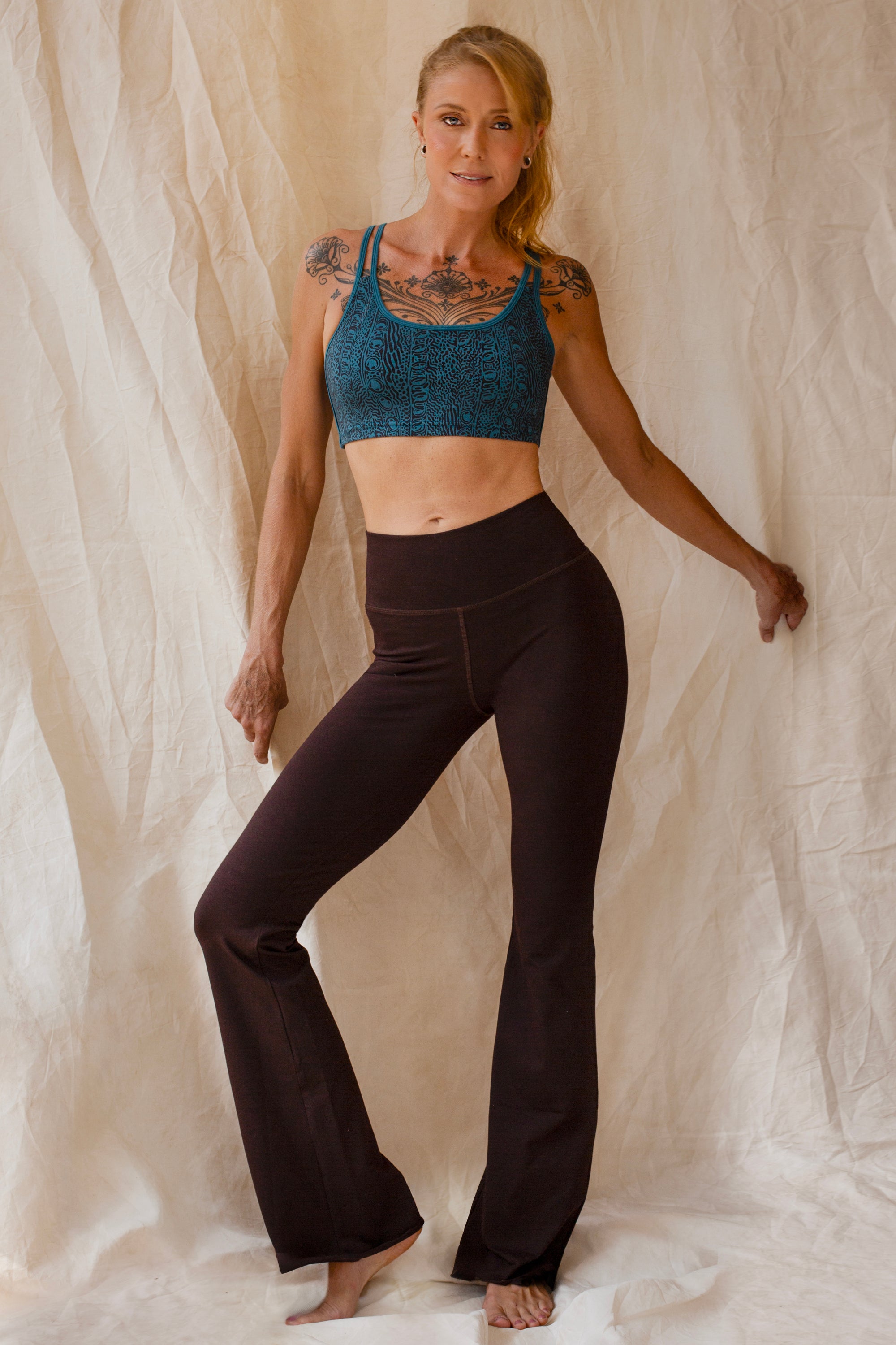 Woman wearing a tosca Argus sports bra and brown flared leggings against a beige curtain background