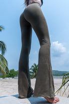 Model wearing olive green color Flares made out of cotton lycra from Funky Simplicity. Shown from the back with palm trees, jungle and a river on the background