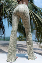 Model wearing Funky Simplicity Flares in Cream Olive Feather print made from cotton lycra - with green palm trees and a river on the background - shown from the back