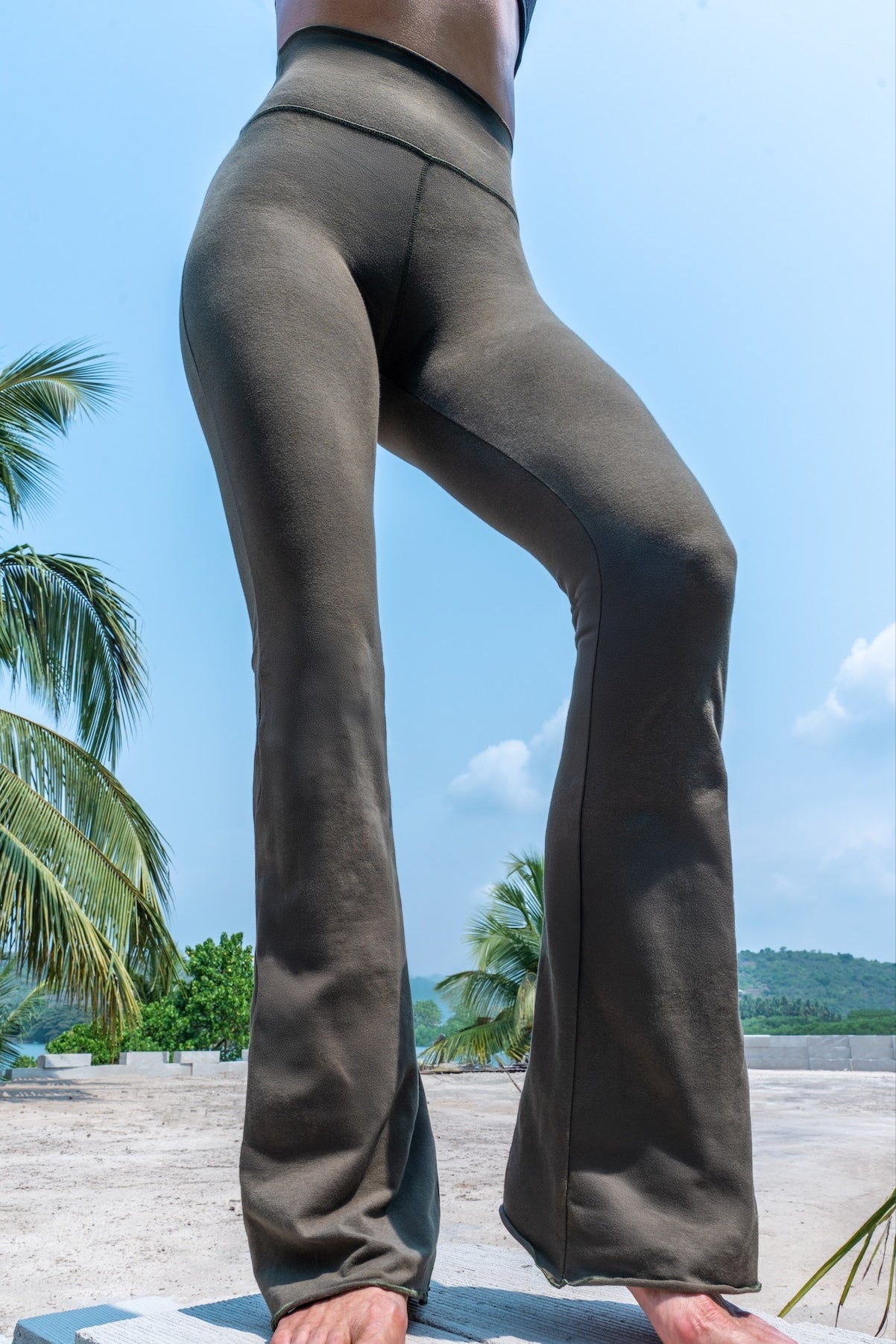 Model wearing olive green color Flares made out of cotton lycra from Funky Simplicity. Shown from the front with palm trees, jungle and mountains on the background