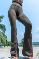 Model wearing olive green color Flares made out of cotton lycra from Funky Simplicity. Shown from the front with palm trees, jungle and mountains on the background