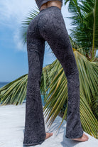 Model wearing Funky Simplicity tribal-print flared leggings in grey black color shown from the back with green palm trees and a blue sky with some clouds on the background.